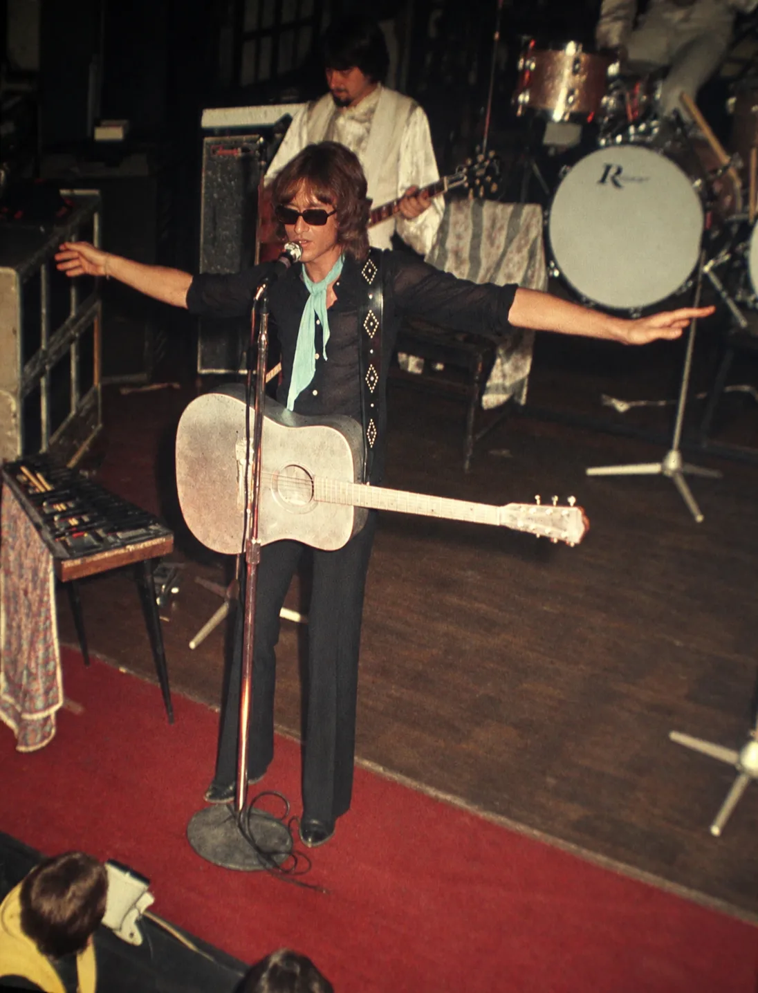 Michel Polnareff sur la scène des Gémeaux le 19 septembre 1969, bras ouverts, guitare acoustique en bandoulière, devant sa batterie Rogers siglée. L'un des concerts marquants du club d'Auderghem à la fin des années 1960.