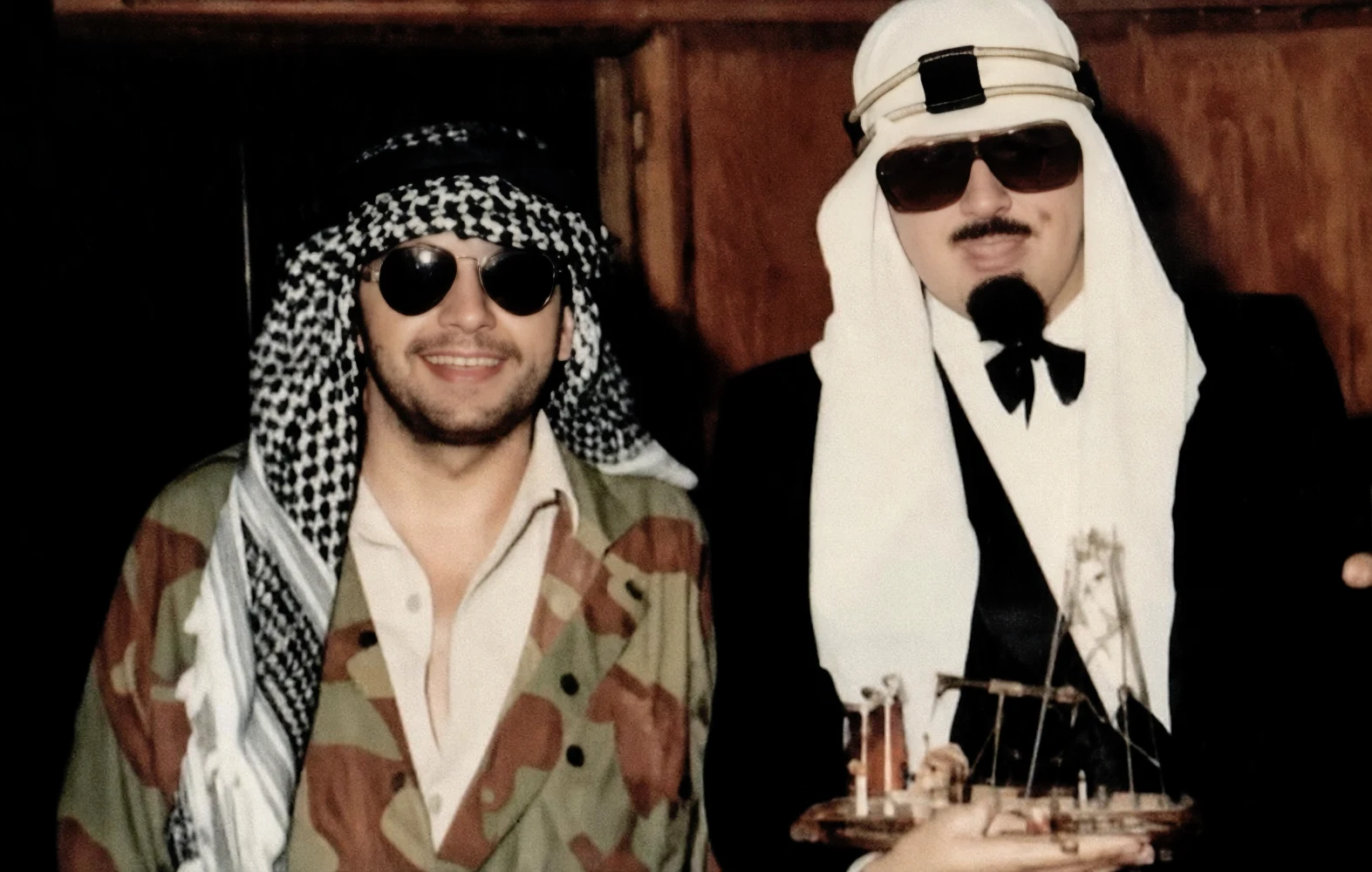 Deux invités en keffiehs et lunettes noires, l'un tenant un boutre miniature, lors de la soirée « Fantasia des Mille et Une Nuits » au Mirano Continental, mercredi 29 septembre 1982.