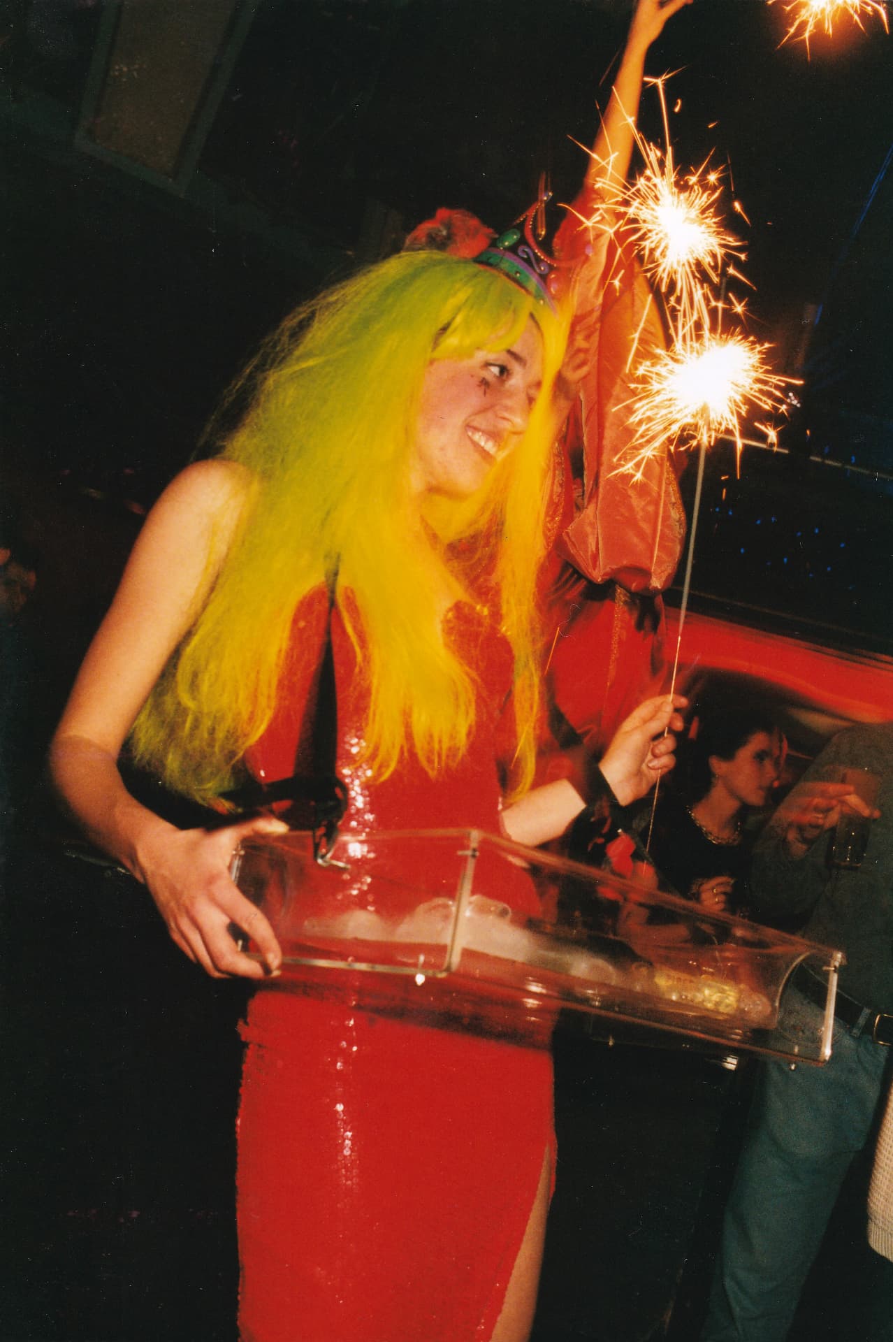 A hostess in a red dress and yellow wig carrying a Perspex vending tray.