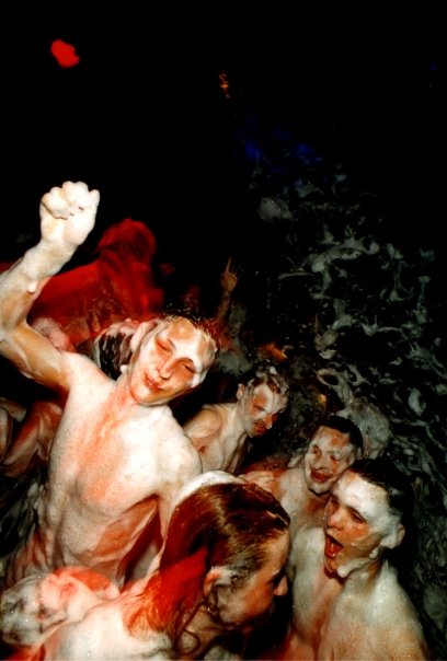 A group of bare-chested dancers in the middle of the foam, under red spotlights.