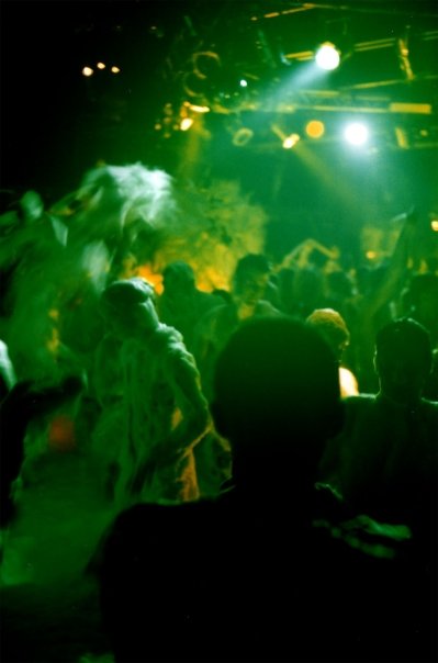The foam spreads across the floor, arms raised in the spotlights.