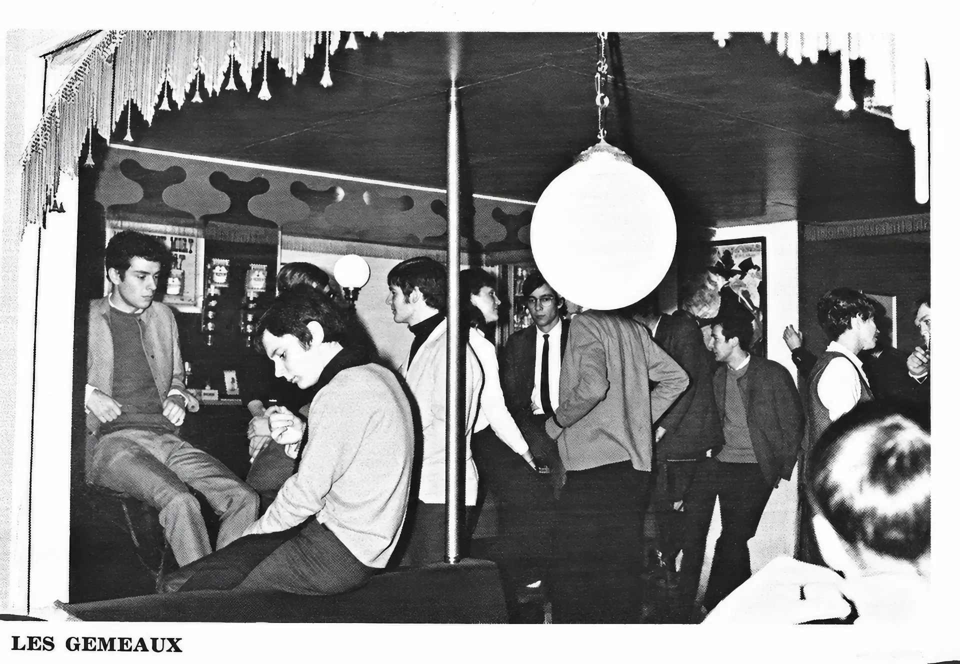 Vue de la salle des Gémeaux : globes lumineux, tentures à franges et clients accoudés autour de la piste. Le décor Belle Époque du club, boulevard du Souverain à Auderghem.