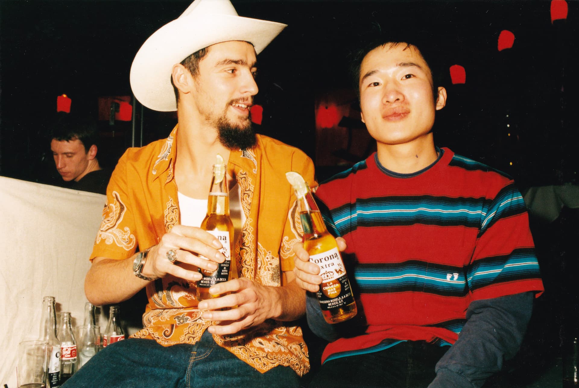 Two guests seated in the room, Corona bottles in hand, under the red lanterns of the Japanese set.