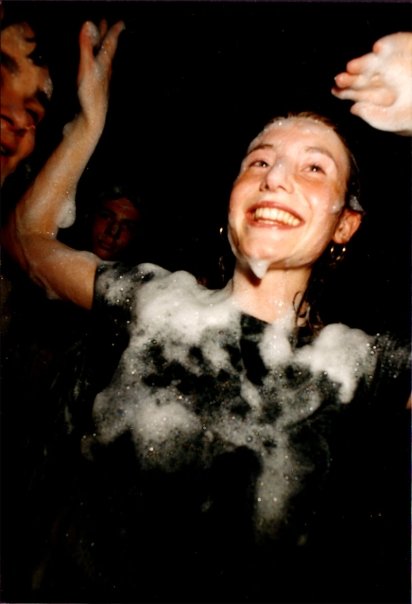 A laughing dancer, foam clinging to her top, arms raised in the crowd.