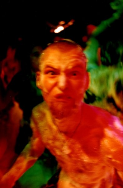 A clubber, bare-chested, pulls a face at the lens in the red and green light.