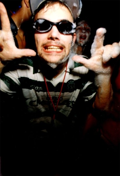 A clubber in a cap and swimming goggles, hands open to the camera.