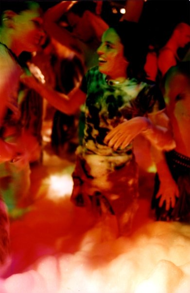 A dancer in a printed dress, in the middle of the floor, in the reds and greens of the club.