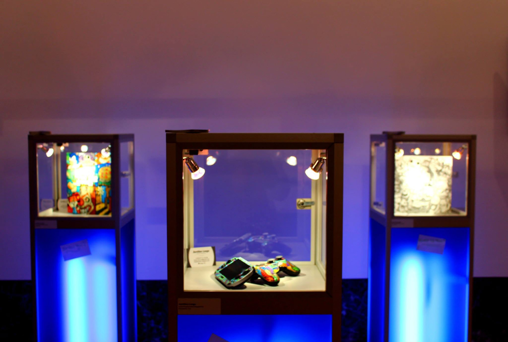 Vitrines éclairées présentant les consoles PlayStation customisées par Aurélien Longo, Art Truc Troc 2014 au Bozar.