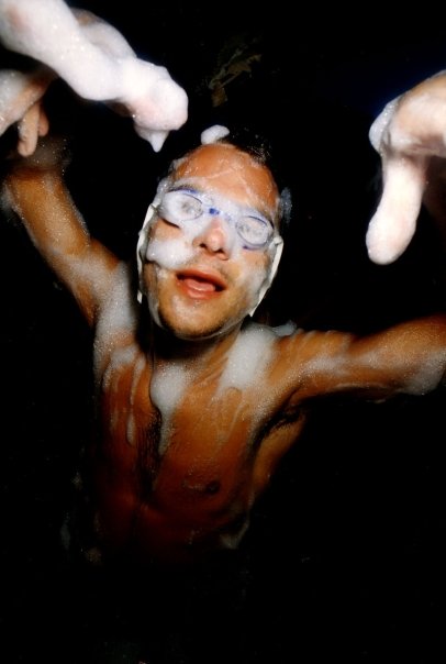 Arms raised and swimming goggles on, a clubber showers the camera with foam.