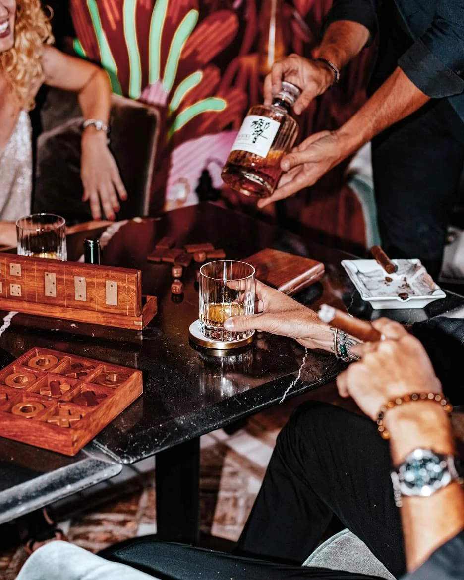 Backgammon, morpion en bois, cigare et whisky japonais servi à table : la soirée s'installe. Au fond, les palmes vertes et roses de la fresque rappellent que tout se passe dans un décor peint à la main.