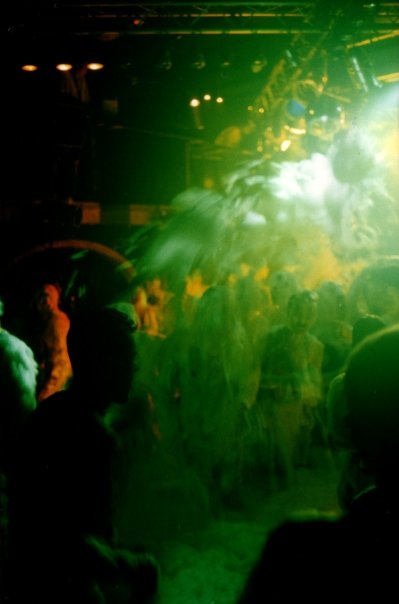 The lance sprays foam above the crowd, green beams backlighting the room.