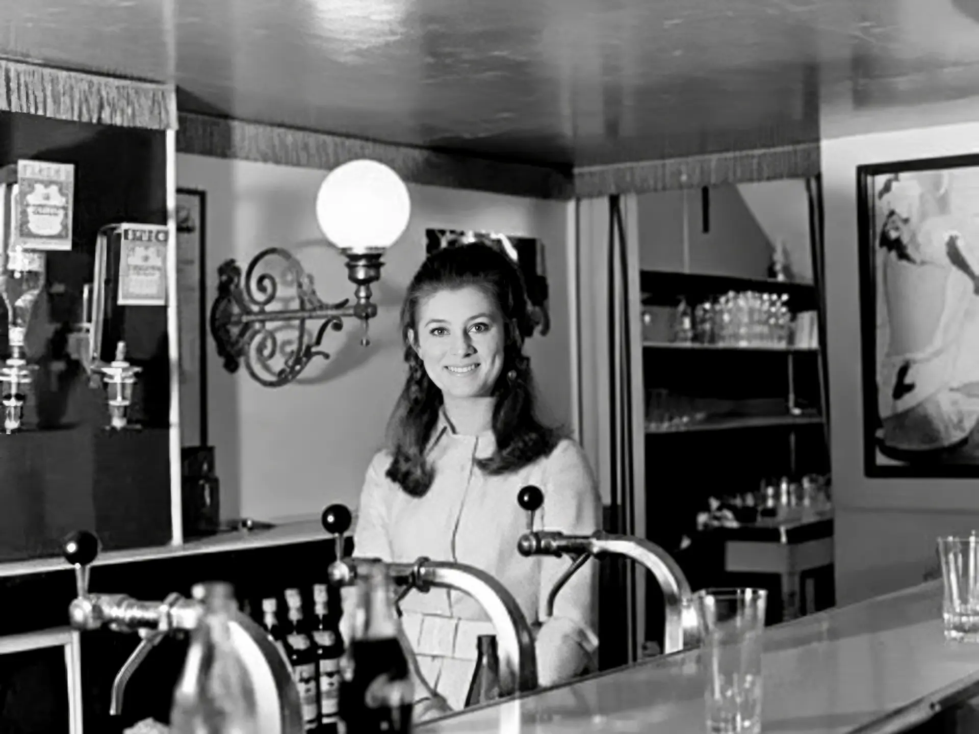 Sheila derrière le bar des Gémeaux, sous les appliques en fer forgé et les lambrequins à franges du décor Belle Époque signé Claude Lombardo.