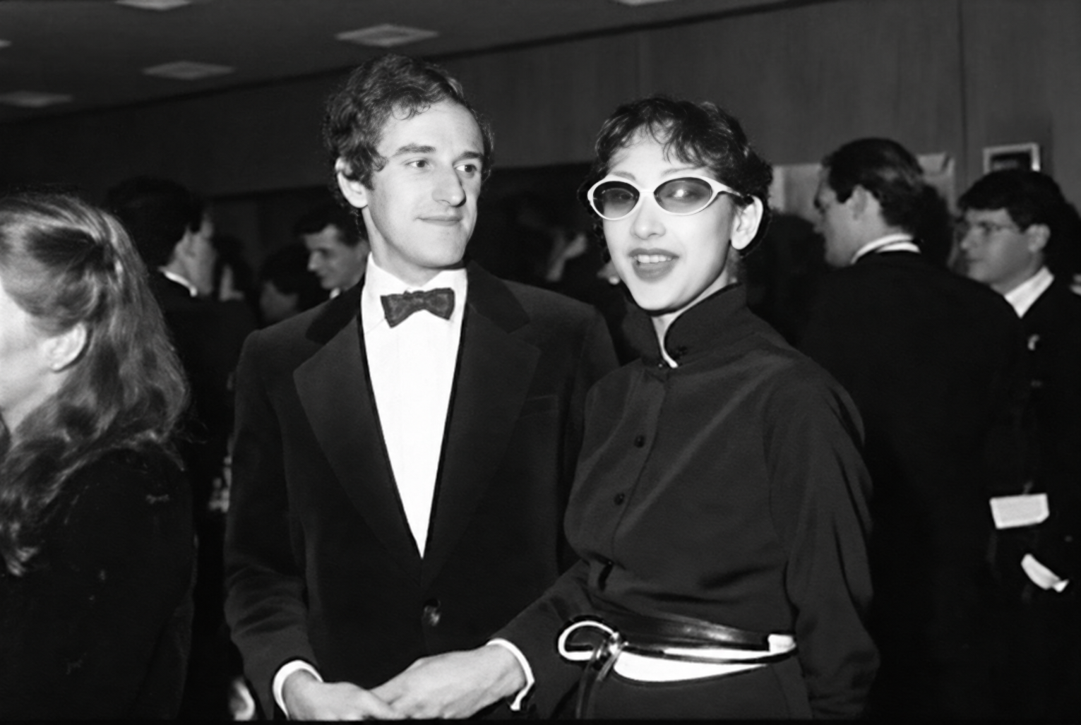 Photographie noir et blanc, format horizontal. Deux hommes en smoking, l'un portant des lunettes de soleil, posent dans l'ambiance nocturne du Mirano Continental.