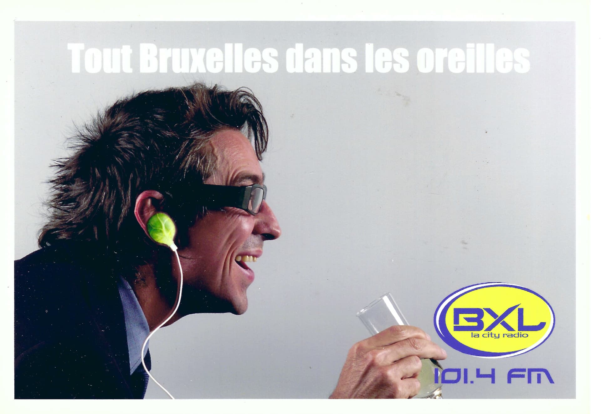 Carl De Moncharline de profil, écouteurs aux oreilles, sur le visuel publicitaire de BXL La City Radio 101.4 FM.