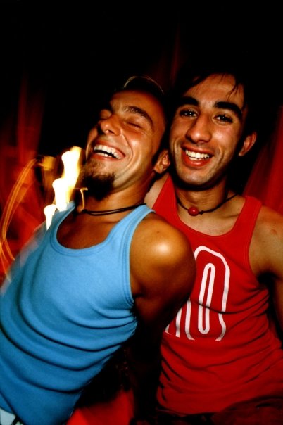 Yorgo, in a blue tank top, and a friend laughing under the red lights of the dance floor.