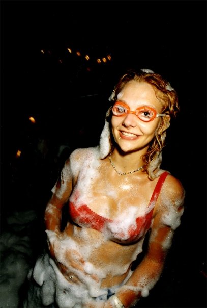 A clubber in orange goggles, covered in foam up to her shoulders.