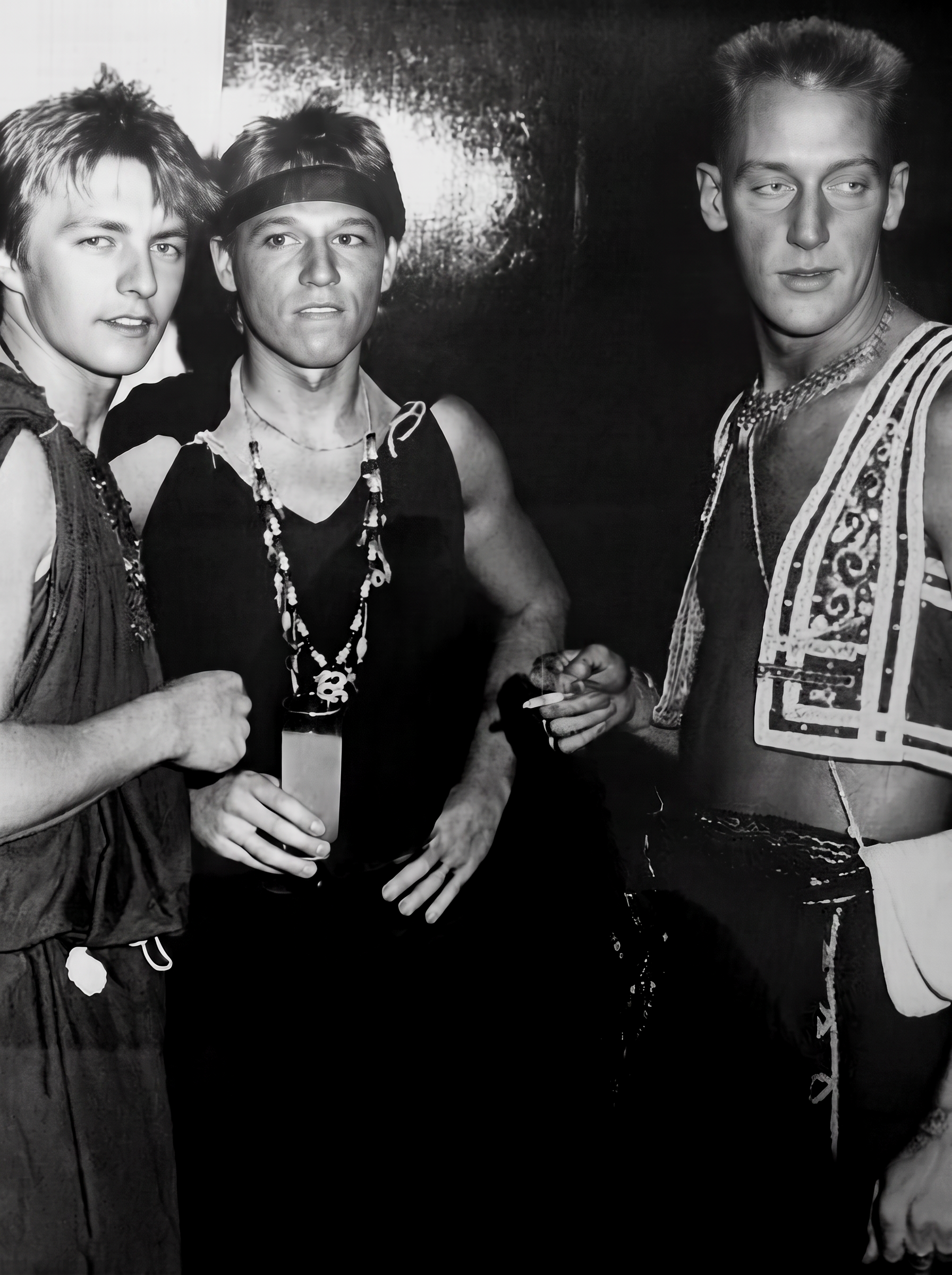 Photographie noir et blanc, format horizontal. Trois clients du Mirano Continental posent en costumes exotiques, colliers et tenues inspirées d'un ailleurs fantasmé, typiques des soirées déguisées du club.